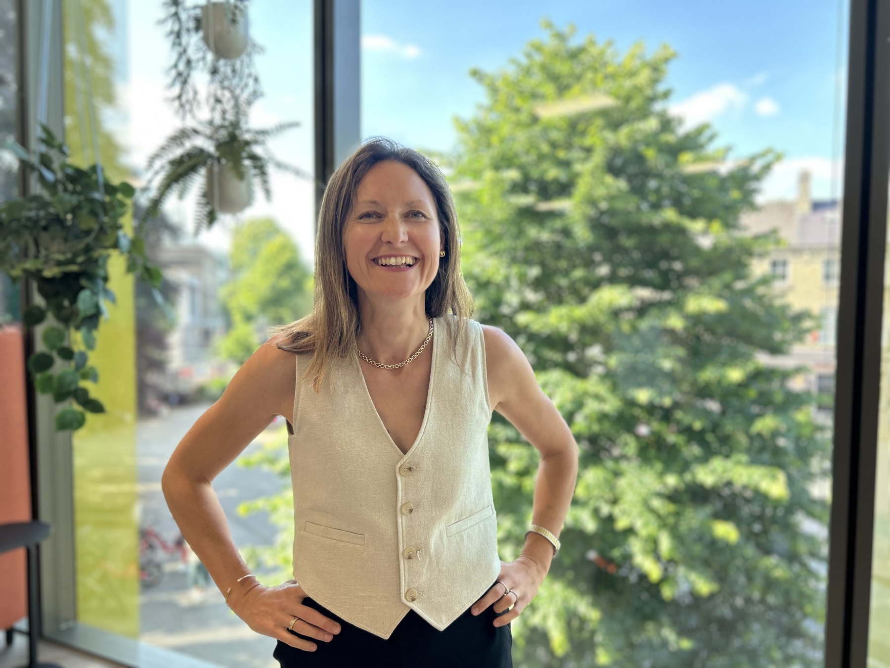 Katy Tuncer, author of HUMANUP, standing by a window with plants and daylight behind her